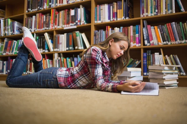 Молодой студент лежит на полу библиотеки и читает — стоковое фото