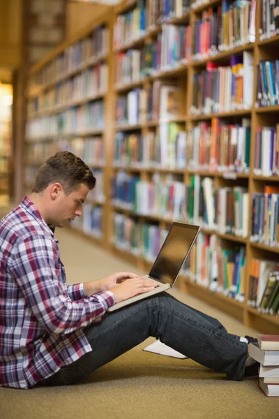 Beau jeune étudiant assis sur le sol de la bibliothèque en utilisant un ordinateur portable — Photo
