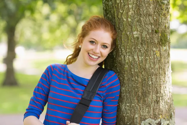快乐的红发学生靠在树上看着相机 — 图库照片