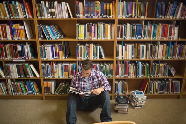 Beau jeune étudiant assis sur le plancher de la bibliothèque livre de lecture — Photo