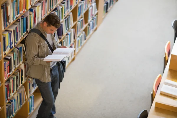 Estudante lendo um livro de prateleira em pé na biblioteca — Fotografia de Stock