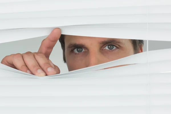 Businessman peeking through blinds in office — Stock Photo, Image