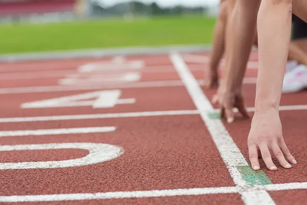 Vista lateral de pessoas cortadas pronto para correr no campo de atletismo — Fotografia de Stock