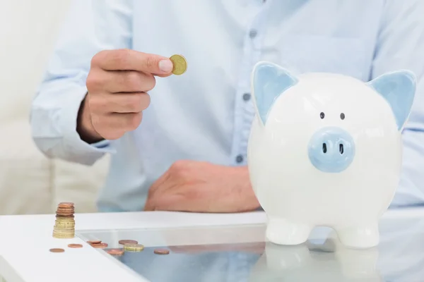 Mid section of a man putting some coins into a piggy bank — Stock Photo, Image
