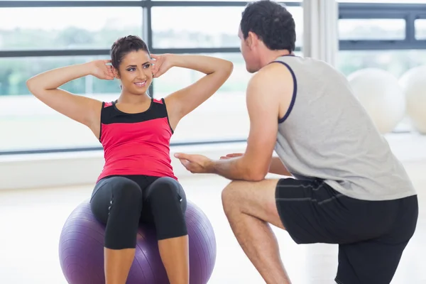 Entrenador ayudando a la mujer a hacer abdominales crujidos en la pelota fitness —  Fotos de Stock