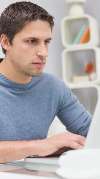 Serious young man using laptop in living room — Stock Photo, Image