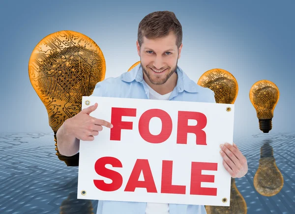 Smiling model holding a for sale sign — Stock Photo, Image