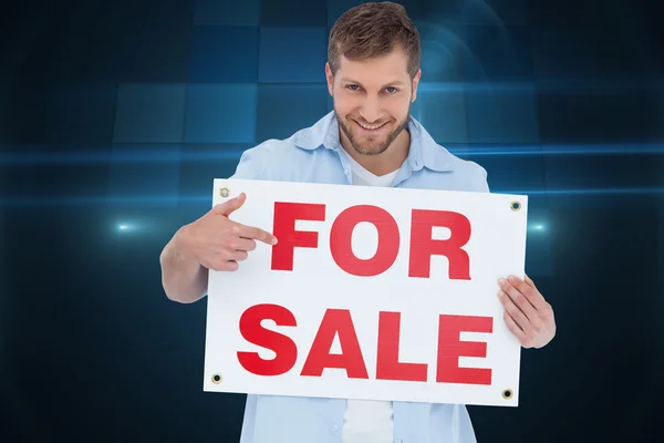 Smiling model holding a for sale sign — Stock Photo, Image