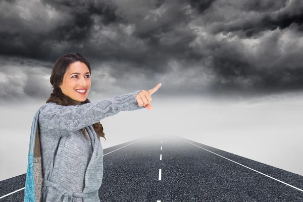 Samengestelde afbeelding van glimlachende brunette dragen winterkleding wijzen op — Stockfoto