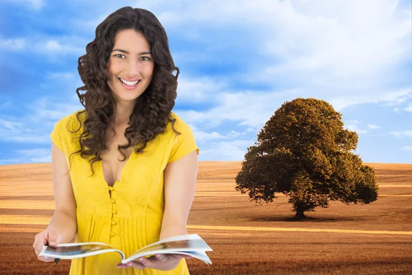Composite image of cheerful curly haired brunette reading magazine — Stock Photo, Image