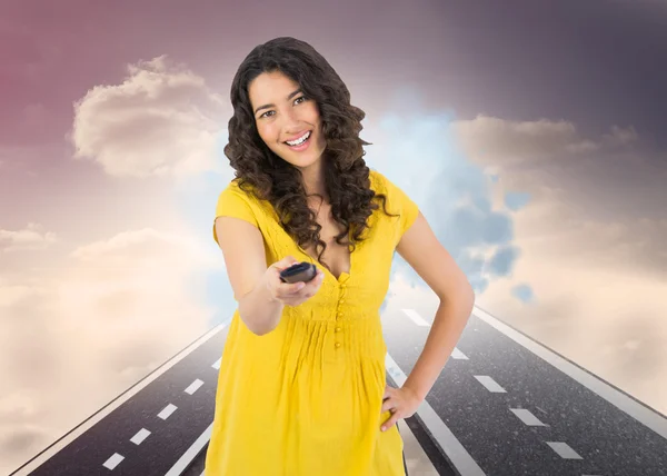 Composite image of smiling curly haired pretty woman changing channel with remote — Stock Photo, Image