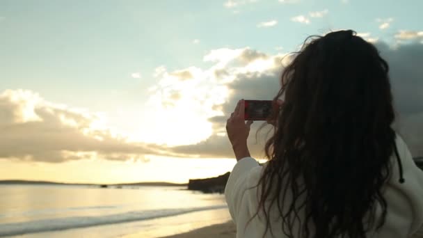 Mulher tirando uma foto do pôr do sol em seu smartphone — Vídeo de Stock