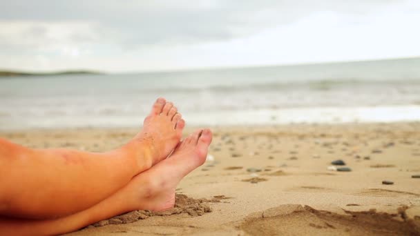 Frauenbeine sitzen am Strand am Wasser — Stockvideo