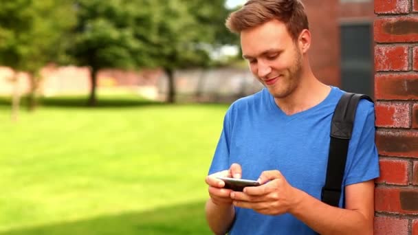 Feliz estudiante mensajes de texto en su teléfono fuera — Vídeo de stock