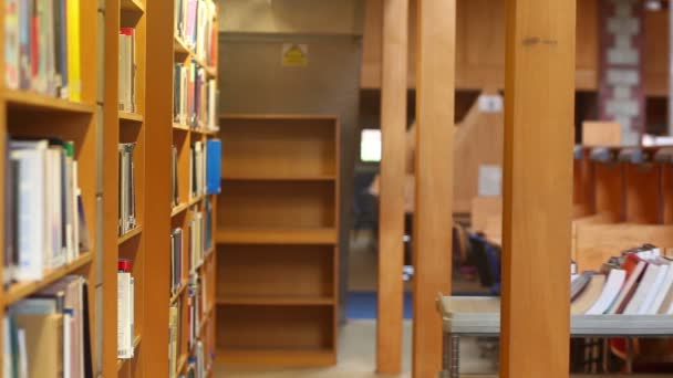 Библиотекарь проталкивает тележку через библиотеку, возвращая книги — стоковое видео