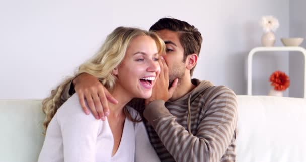 Hombre susurrando un secreto a su novia en el sofá — Vídeo de stock