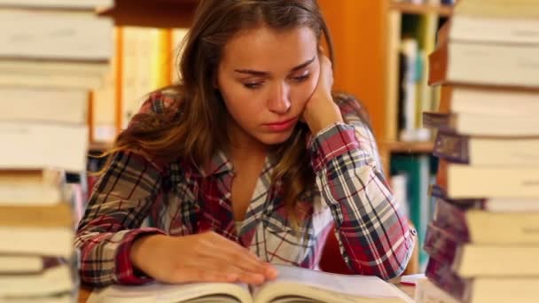 Estudiante cansado estudiando en la biblioteca rodeado de libros — Vídeo de stock