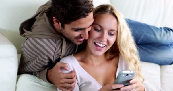 Happy young couple sitting on the couch while girlfriend is texting — Stock Video