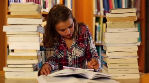 Student studuje a zapisování poznámek v knihovně obklopena knihami — Stock video