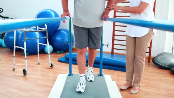 Физиотерапевт помогает пациенту ходить с параллельными брусьями — стоковое видео