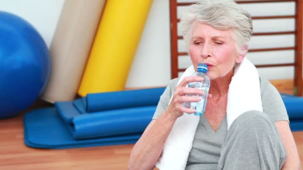 Mujer mayor sentada en el suelo bebiendo agua — Vídeos de Stock