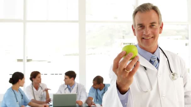 Mature doctor looking at camera holding an apple — Stock Video