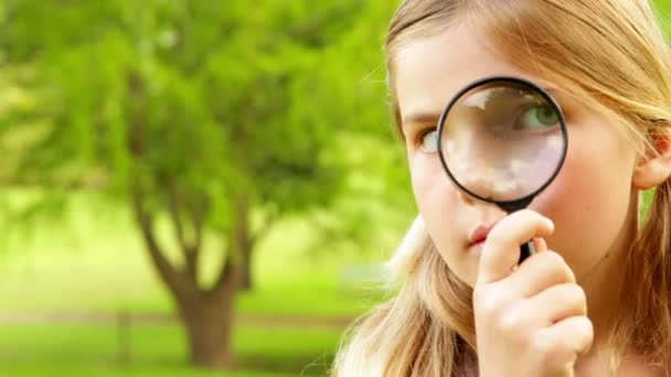 Carino bambina utilizzando lente di ingrandimento nel parco — Video Stock