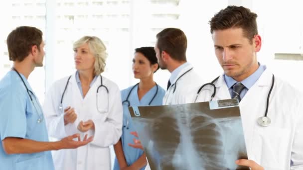 Ernsthafter Arzt hält Röntgengerät in der Hand, während Mitarbeiter hinter ihm stehen — Stockvideo