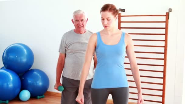 Physiotherapist showing elderly man how to lift weights — Stockvideo