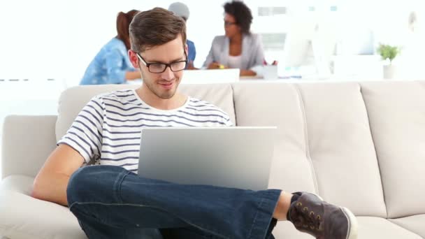 Diseñador guapo sentado en el sofá trabajando en el ordenador portátil — Vídeos de Stock