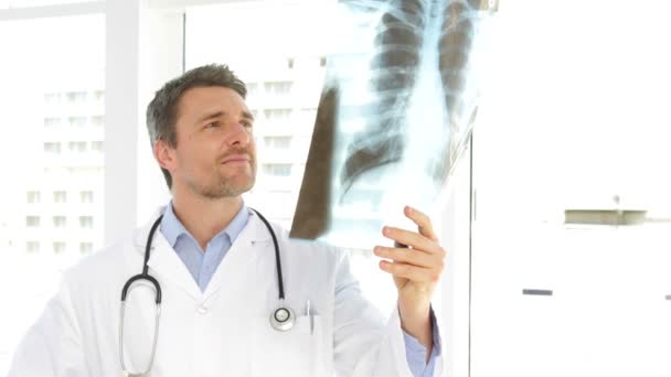 Doctor estudiando una radiografía y mirando a la cámara — Vídeos de Stock