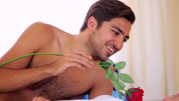 Мужчина щекочет свою блондинку розой на кровати — стоковое видео
