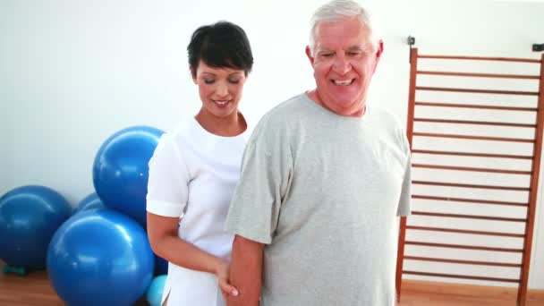 Happy physiotherapist helping elderly patient lift hand weights — Stock Video