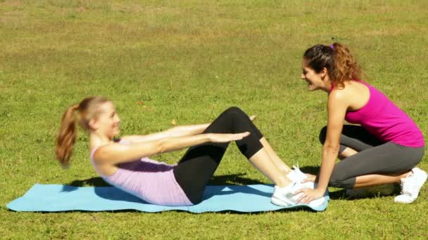 Woman doing sit ups in the park with her trainer — Stock Video