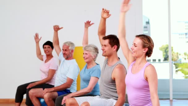 Groupe de fitness assis sur des boules d'exercice étirant les bras — Video