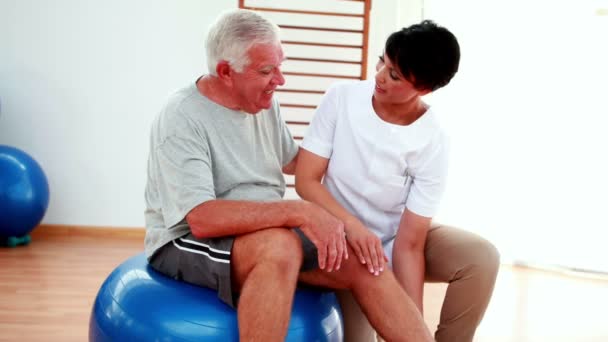 Fisioterapeuta sonriente ayudando al paciente anciano a doblar la rodilla — Vídeos de Stock