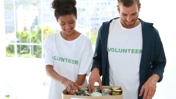 Счастливая волонтерская команда упаковывает коробку для пожертвований продуктов — стоковое видео