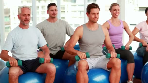 Fitness group sitting on exercise balls lifting hand weights — Stock Video