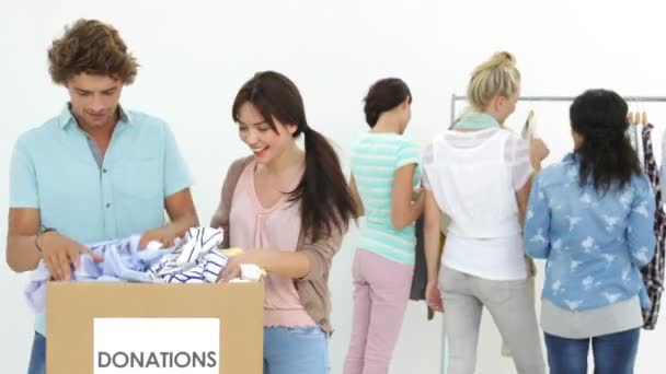 Squadra di lavoratori felici che passano attraverso la scatola delle donazioni di vestiti — Video Stock