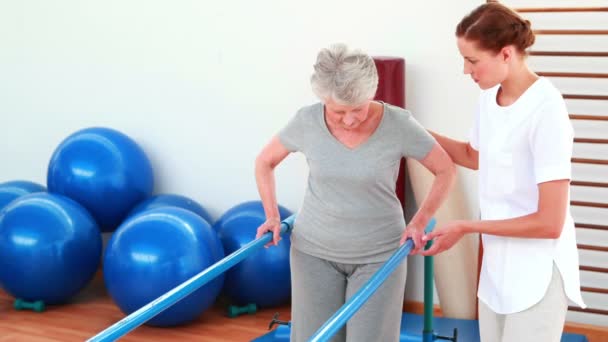 Physical therapist helping patient walk with parallel bars — Stock Video