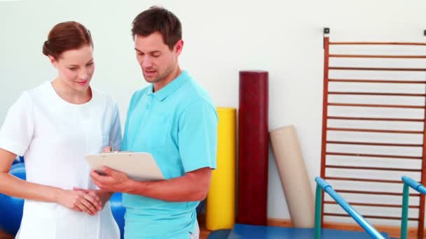 Smiling physical therapists looking at clipboard — Stock Video
