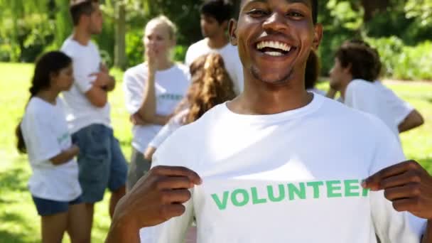Knappe vrijwilligers tonen zijn tshirt naar camera — Stockvideo
