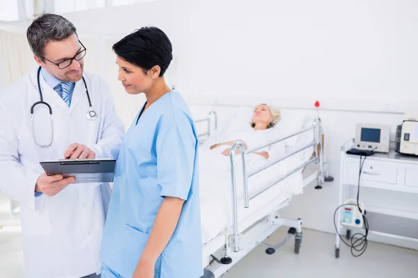 Médicos discutindo relatos com pacientes em segundo plano — Fotografia de Stock