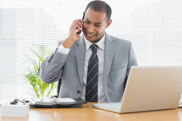 Lachende zakenman met laptop met behulp van mobiele telefoon — Stockfoto