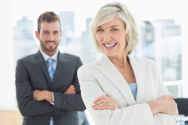 Mature businesswoman and young man with arms crossed clipart