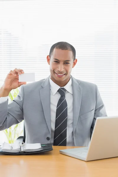 Confident well dressed man with business card at office desk — Stock Photo, Image