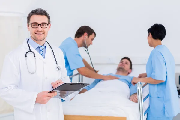 Doctor holding reports with patient and surgeon in background — Stock Photo, Image