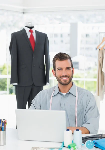 Diseñador de moda masculino sonriente usando el ordenador portátil en el estudio —  Fotos de Stock