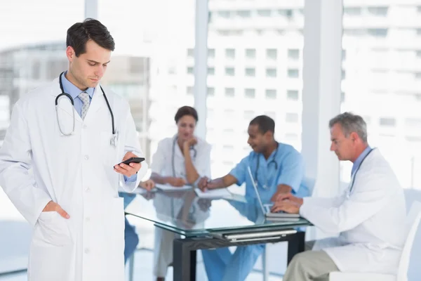 Doctor text messaging with group around table in hospital — Stock Photo, Image