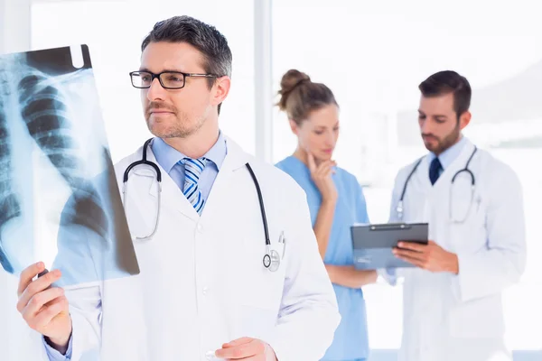 Médico masculino examinando rayos X con colegas detrás — Foto de Stock